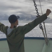 Osama Alian stands on a boat with his arms raised. 