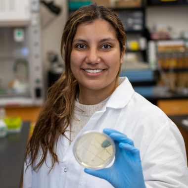 Sarah Gonzalez Henao holds up a petri dish. She is standing in her lab. 